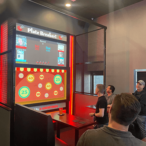 A group of friends engrossed in a competitive game of digital darts at Corky's Gaming Bistro.